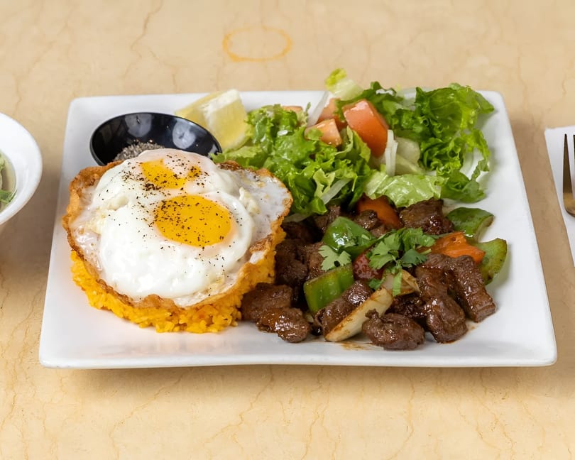 Savory beef stir-fry with bell peppers, onions, cilantro, fried eggs, yellow rice, and a side salad.